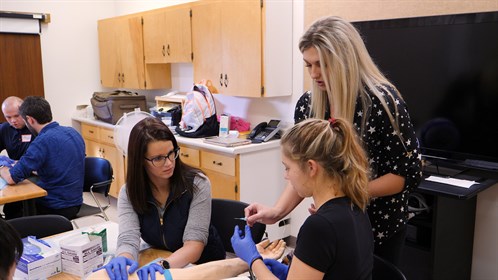 Bailey (standing) teaches IV Starts to healthcare students from Calgary at an RhPAP Skills Day event held at the Milk River Health Centre.